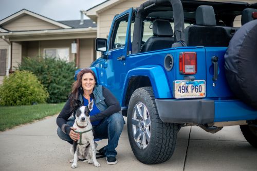 Dr. Wendy Iszler crouching with a black-and-white dog beside a blue Jeep